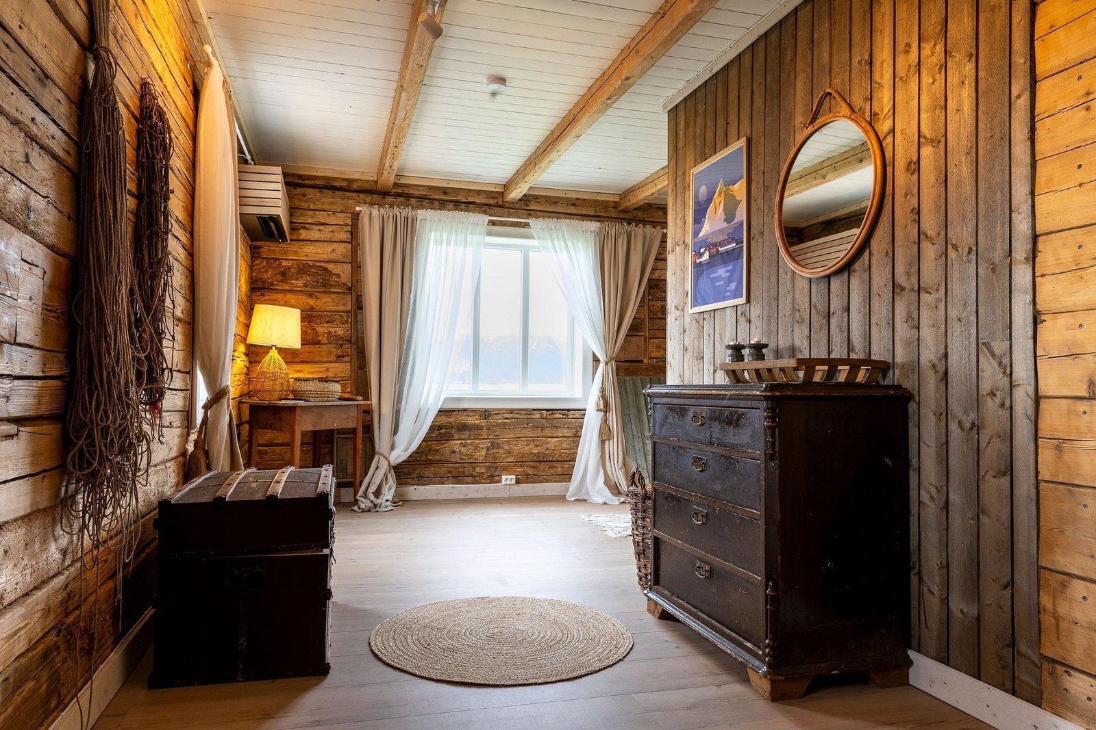 Log-walled guest room with an old sea chest, a dark wooden dresser, fishing nets on the wall and a bright window